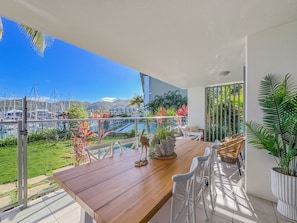 A balcony with a wooden table, white chairs, and a decorative bird sculpture. - Blue on Blue Apartment 1011 (Nelly Bay)