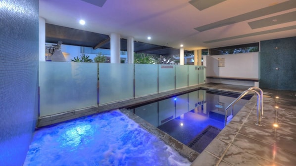 A modern indoor pool with glass walls, a hot tub, and a tiled floor.