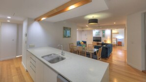 A modern kitchen with a central island, a dining area with wooden chairs, and a living room with a sofa and TV. - Maggies Beachfront Apt. 4 (Horseshoe Bay)