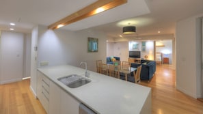 A modern kitchen with a central island, a dining area with wooden chairs, and a living room with a sofa and TV.