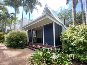 A house with a covered porch, surrounded by lush greenery and palm trees. - Canopy Chalet 4 (Nelly Bay)