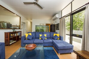 A living room with a sectional sofa, a glass coffee table, a fish tank, and a view of the outdoors. - Sunbird Retreat (Horseshoe Bay)