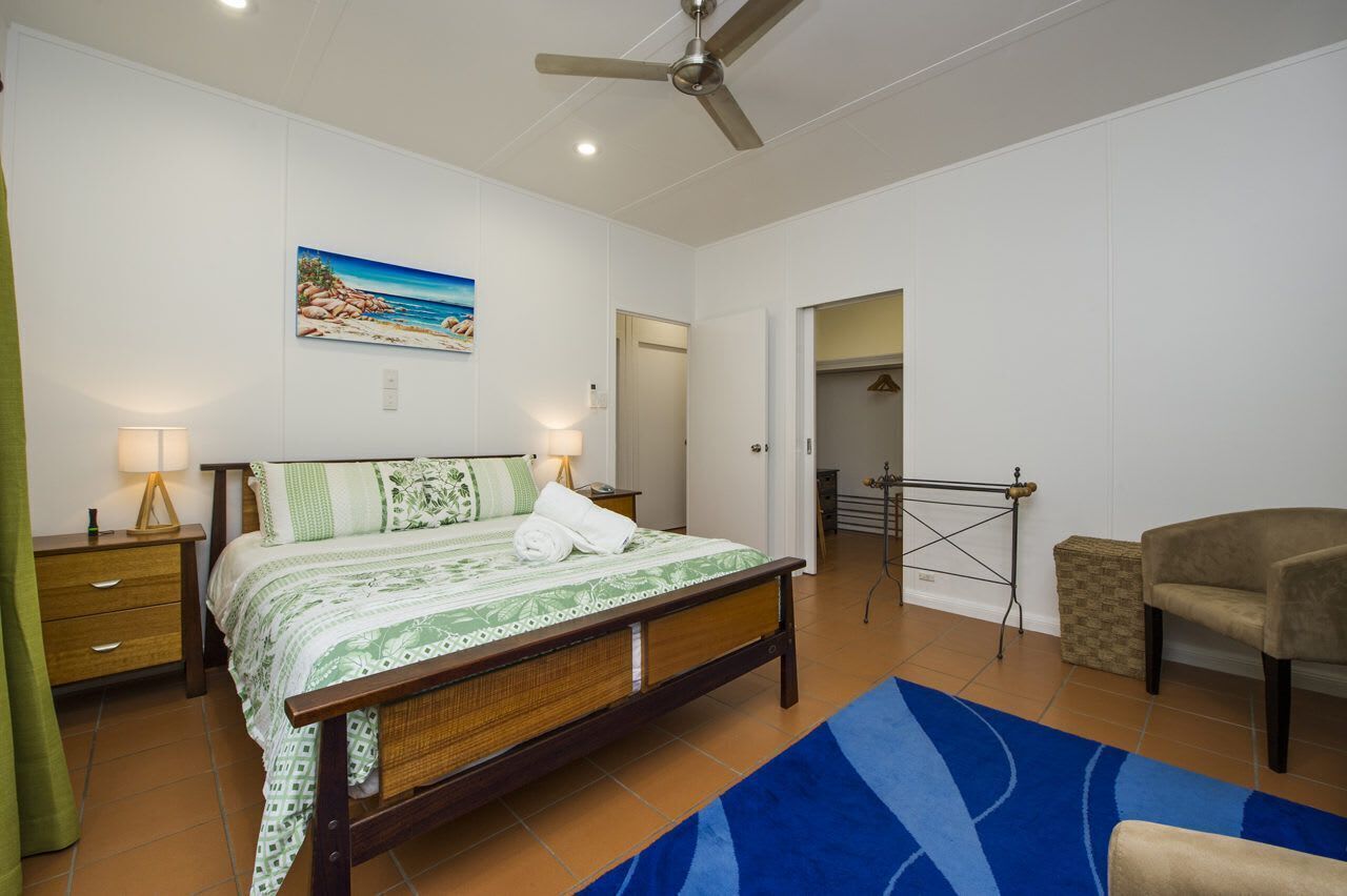 Une chambre à coucher avec un lit, des lampes de chevet, un ventilateur de plafond, un tableau, une chaise et un tapis bleu.