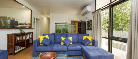 A living room with a sectional sofa, a glass coffee table, a fish tank, and a view of the outdoors.