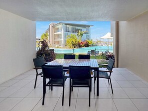 Varanda com mesa e cadeiras, com vista para uma piscina e um edifício.