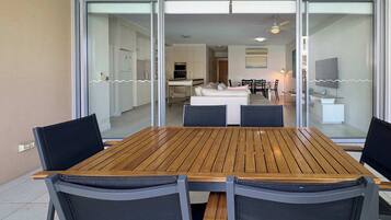 A dining area with a wooden table and chairs, a kitchen in the background, and a sliding glass door leading to a living space.