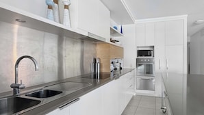 A modern kitchen with stainless steel appliances, a double sink, and white cabinetry. - Blue on Blue Apartment 813 (Nelly Bay)
