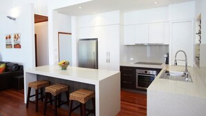 A modern kitchen with white cabinetry, a stainless steel refrigerator, a built-in oven, and a large island with stools.