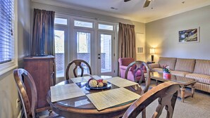 A dining area with a round table, chairs, and a ceiling fan. There is a sofa and a lamp in the adjacent living room. - Resort-Style Condo/Suite on Golf Course w/ Pool! (Spring Lake)