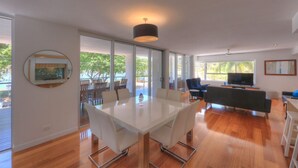 Una sala de estar moderna con una mesa de vidrio, un sofá, un televisor y un ventanal grande.
