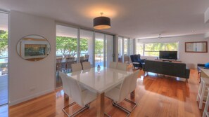 A modern living room with a glass dining table, a sofa, a TV, and a large window.