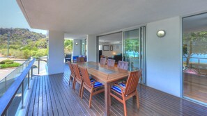 A wooden deck with a dining table and chairs, a glass railing, and a view of the outdoors.