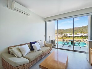 Un salon moderne avec un canapé en osier, une table basse en bois et une grande porte-fenêtre coulissante donnant sur un espace piscine.