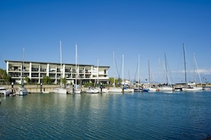 A marina with multiple sailboats docked in front of a modern building with multiple floors and balconies.