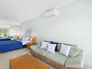 A hotel room with a bed, a sofa, a coffee table, and an air conditioning unit.