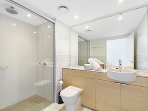 A modern bathroom with a glass-enclosed shower, a white toilet, and a vanity with a sink and mirror.