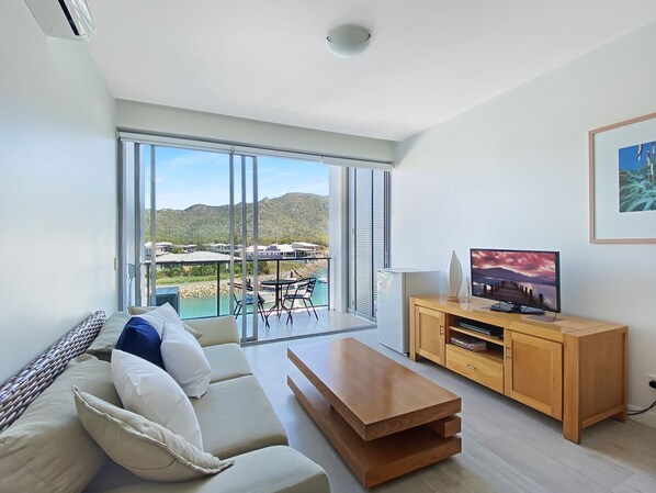 A modern living room with a sofa, TV stand, and a balcony with a view of the sea.
