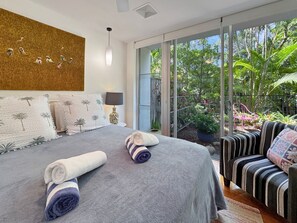 A modern bedroom with a large bed, a balcony with plants, and a view of the outdoors.
