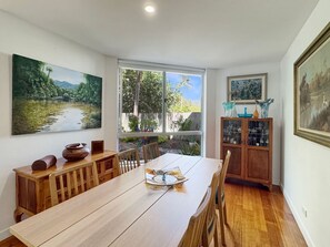 Un comedor con una mesa de madera, sillas, un armario con puertas de cristal y un ventanal con vistas al verdor.