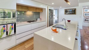A modern kitchen with white cabinetry, a central island, stainless steel appliances, and a view of the outdoors. - Maggies Beachfront Apt. 2 (Horseshoe Bay)