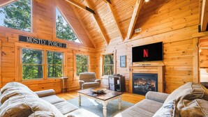 L’intérieur d’un chalet confortable en bois, avec une cheminée, des fauteuils confortables et un téléviseur.
