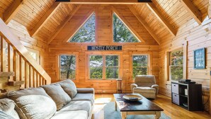 L’intérieur d’un chalet en bois chaleureux et accueillant, avec un canapé, des fauteuils, une table basse et une pancarte sur laquelle on peut lire : « PRINCIPALEMENT PORCHE ».