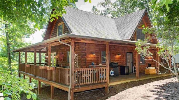 Une cabane en bois avec une véranda, une cheminée et une grande fenêtre.