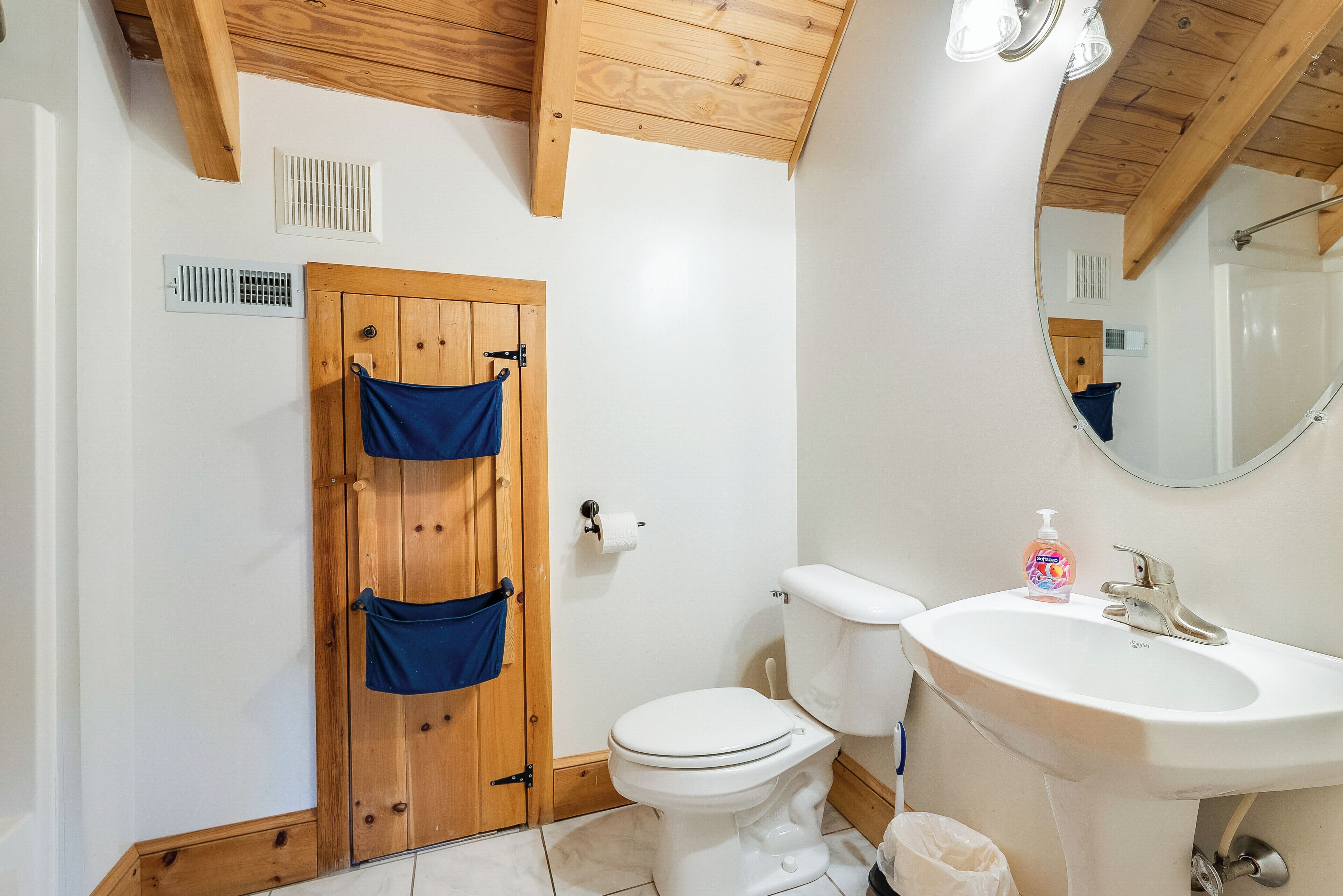 A bathroom with a wooden door, a toilet, a sink, and a mirror.