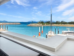 A marina with boats docked, a rocky breakwater, and a clear blue sky.