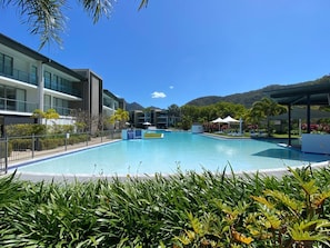 A swimming pool with lounge chairs, a covered seating area, and a building with balconies.