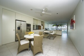 A modern kitchen with a dining area, a ceiling fan, and a view of the outdoors. - Blue on Blue Apartment 912 (Nelly Bay)