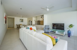 A modern living room with a white sofa, a TV, and a dining area in the background. - Blue on Blue Apartment 912 (Nelly Bay)