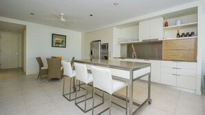 Een moderne keuken met een centraal eiland, witte kasten en een eethoek met rieten stoelen.