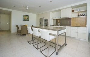 A modern kitchen with a central island, white cabinetry, and a dining area with wicker chairs. - Blue on Blue Apartment 912 (Nelly Bay)
