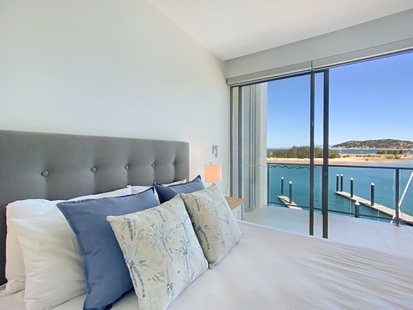 A bedroom with a large bed, a view of the sea, and a balcony.