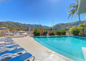 Ein Swimmingpool mit Liegestühlen, umgeben von tropischen Pflanzen und Bergen im Hintergrund.