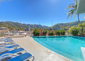 A swimming pool with lounge chairs, surrounded by tropical plants and mountains in the background.