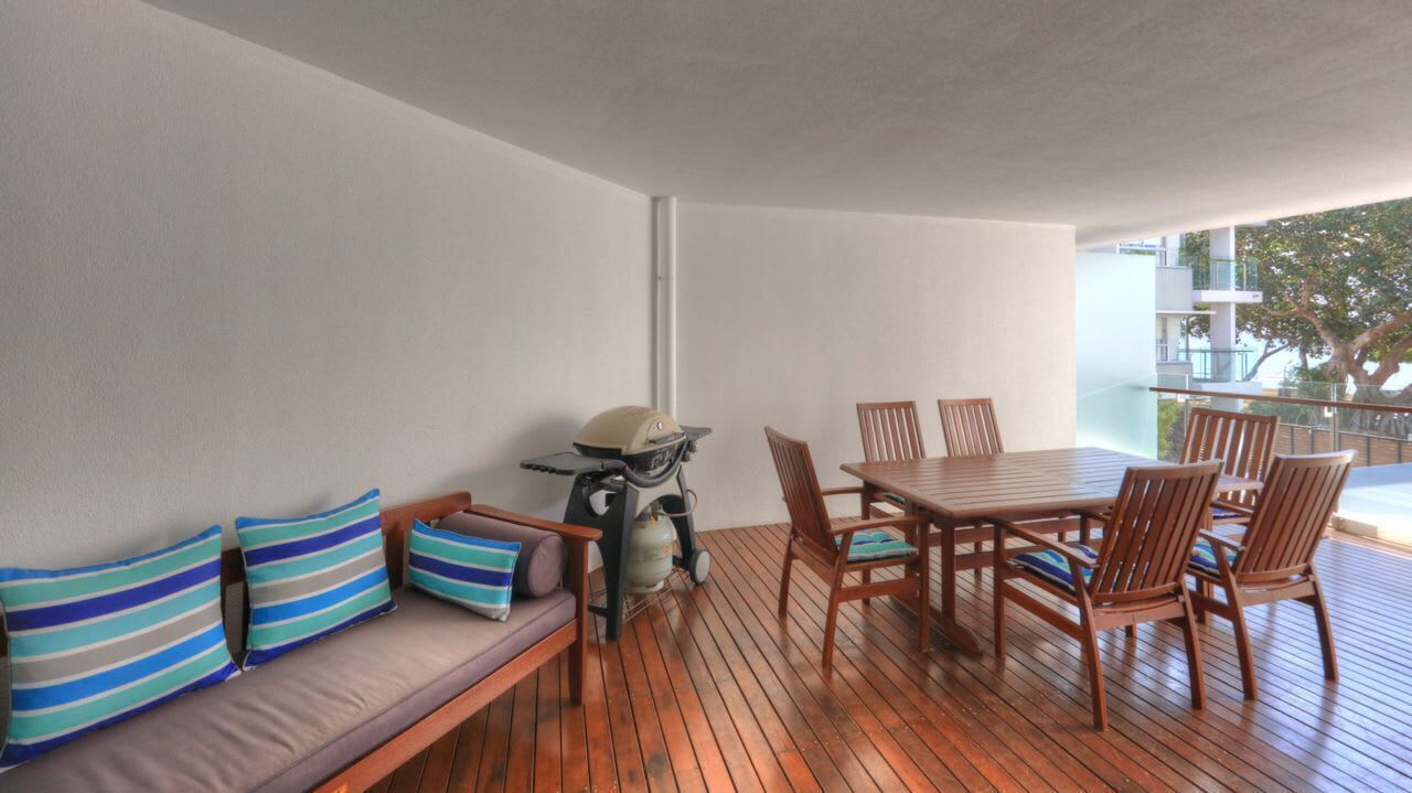 A balcony with a wooden table and chairs, a sofa with striped cushions, and a scooter.
