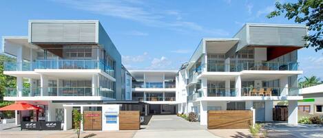 A modern multi-story hotel with balconies, a covered entrance, and a clear sky.