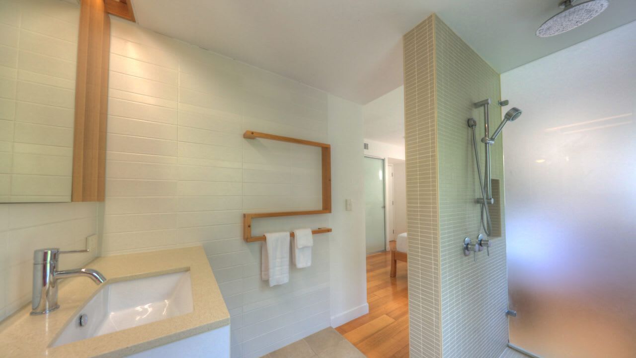Ein Badezimmer mit Waschbecken, Spiegel, Handtuchhalter, Dusche und Holzelementen.