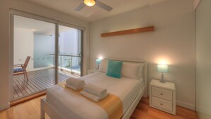 Een slaapkamer met een bed, nachtkastje, bedlamp, balkon met een stoel en een plafondventilator.
