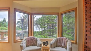 Una habitación acogedora con dos sillones orientados a un gran ventanal con vistas a un bosque. Una pequeña mesa de madera se encuentra entre los sillones, sosteniendo unos binoculares y una cámara.