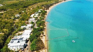 An aerial view of a coastal area with a beach, buildings, and clear blue water.