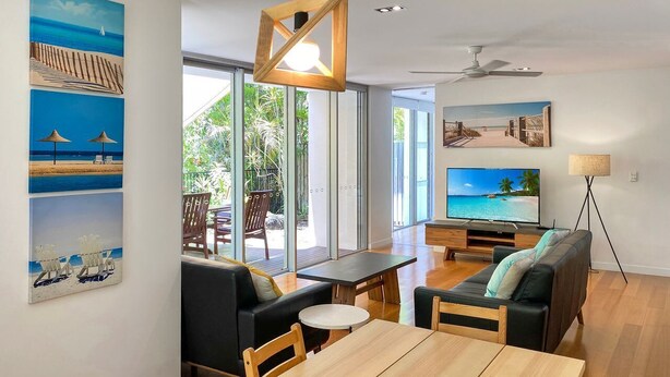A modern living room with a wooden dining table, black sofas, and a TV.