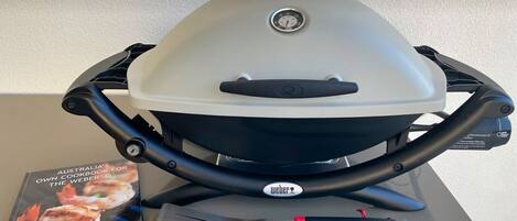 Ein Weber-Grill mit Kochbuch, Pfanne und Grillzange.