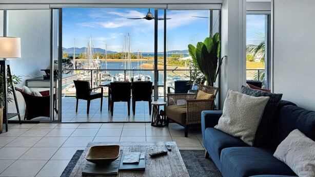 A modern living room with a large sliding glass door leading to a balcony with a marina view.
