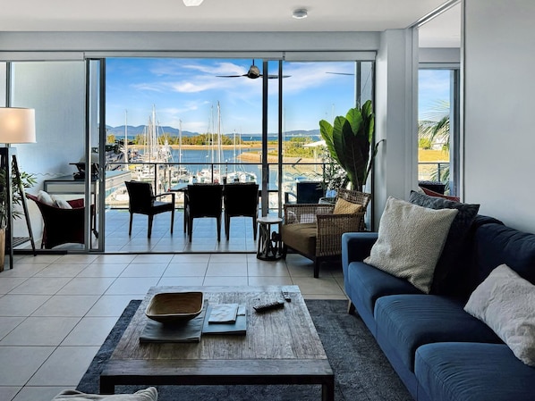Ein modernes Wohnzimmer mit einem großen Schiebeglasfenster, das auf einen Balkon mit Blick auf eine Marina führt.