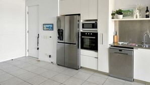 A modern kitchen with stainless steel appliances, white cabinetry, and a tiled floor.