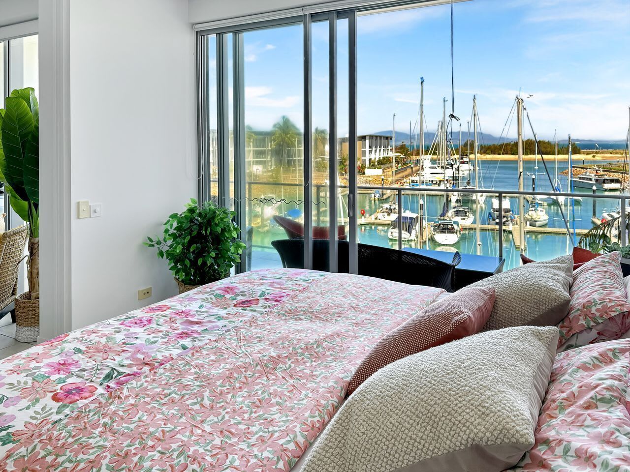 A bedroom with a large bed, a view of a marina with boats, and a potted plant.