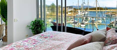 A bedroom with a large bed, a view of a marina with boats, and a potted plant.